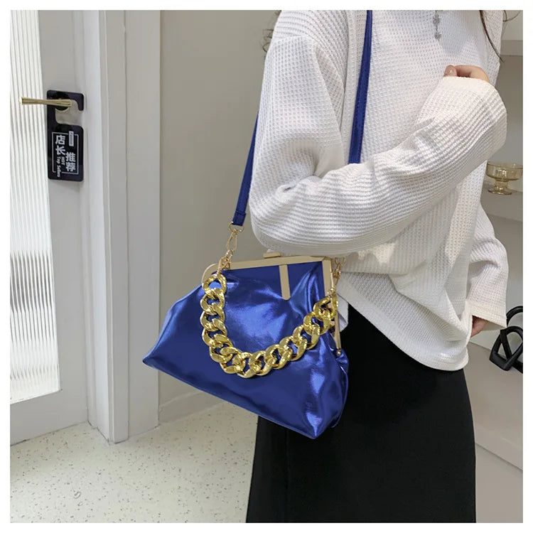 Person holding a blue Carauana UNIU Aurora Clutch handbag with a gold chain handle indoors.
