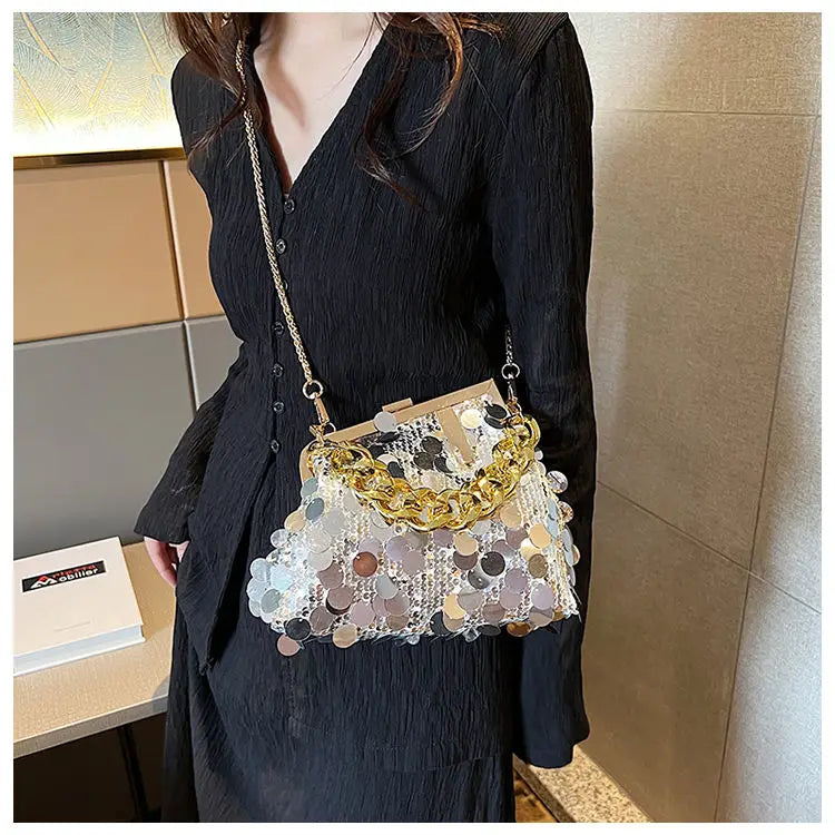 Person wearing a black outfit with a decorative handbag featuring gold chains and multicolored sequins.