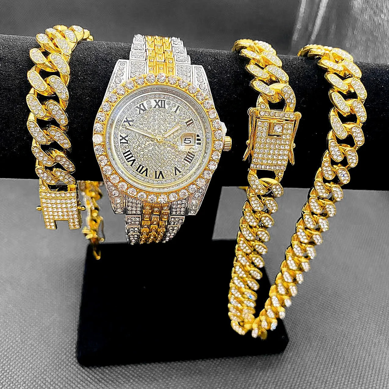 Gold watch and bracelet set on a black stand with a gray background